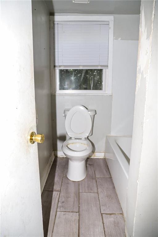 full bath featuring a tub, wood finish floors, and toilet