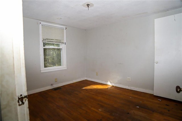 empty room featuring dark wood finished floors, visible vents, and baseboards