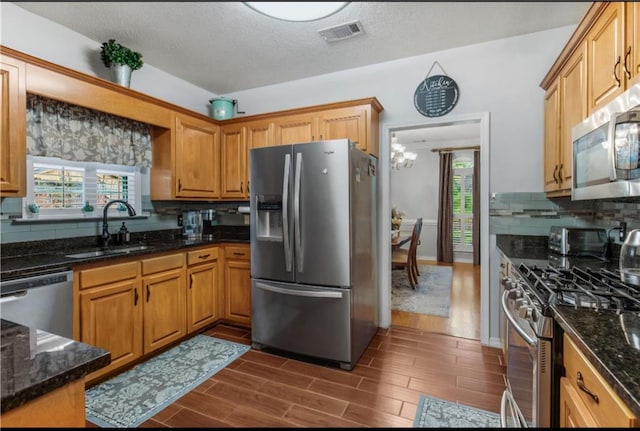 kitchen with tasteful backsplash, dark stone counters, appliances with stainless steel finishes, sink, and dark wood-type flooring