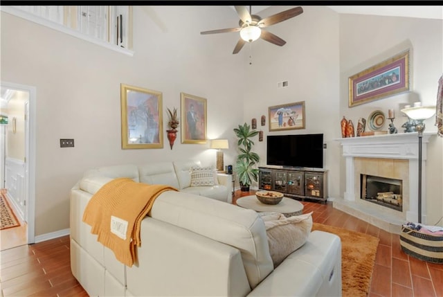 living room featuring high vaulted ceiling, ceiling fan, light wood-type flooring, and a tile fireplace