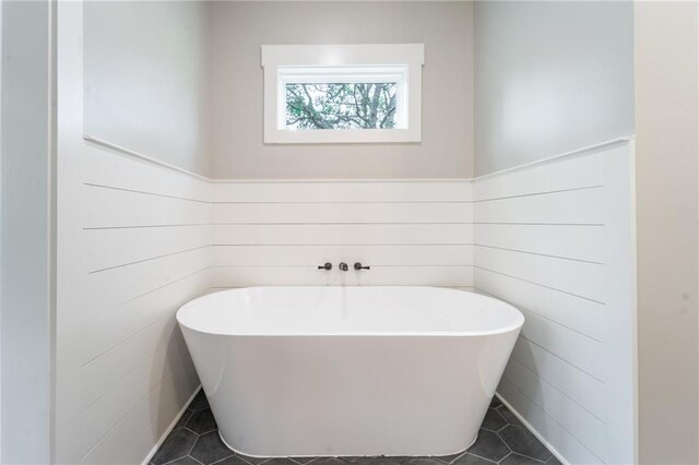 bathroom with a wainscoted wall, tile patterned flooring, and a freestanding bath