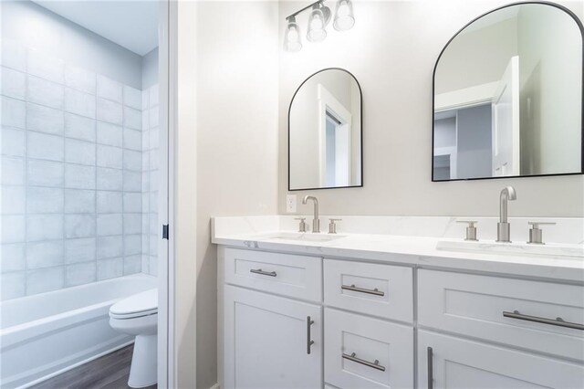 bathroom with double vanity, a sink, toilet, and wood finished floors