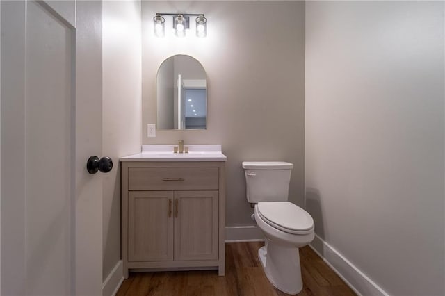 half bath featuring baseboards, toilet, vanity, and wood finished floors