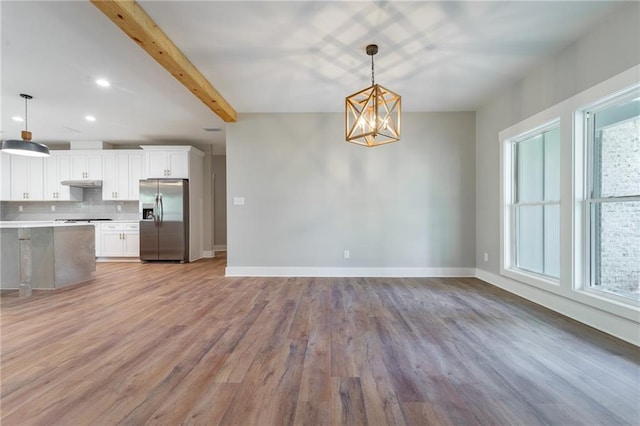 kitchen featuring light countertops, beamed ceiling, under cabinet range hood, stainless steel fridge with ice dispenser, and a notable chandelier