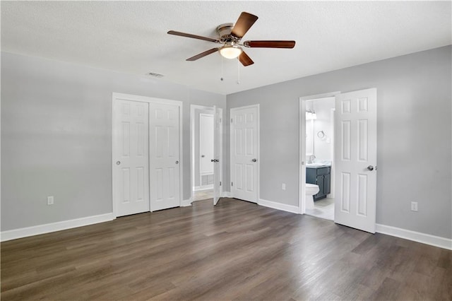 unfurnished bedroom with ceiling fan, dark hardwood / wood-style floors, a textured ceiling, and ensuite bath