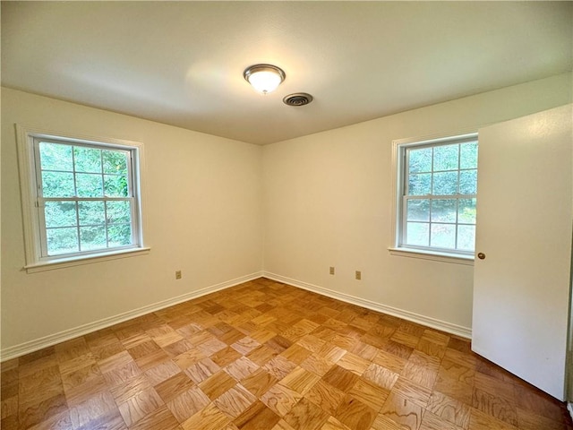 unfurnished room with a wealth of natural light, visible vents, and baseboards