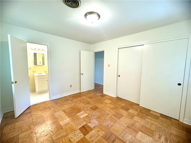 unfurnished bedroom featuring a closet, ensuite bath, visible vents, and baseboards