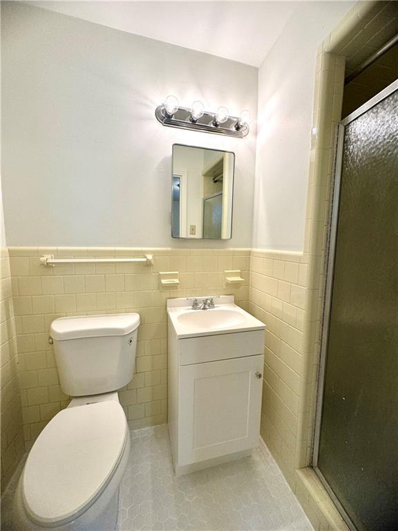 full bath featuring a stall shower, wainscoting, vanity, and toilet