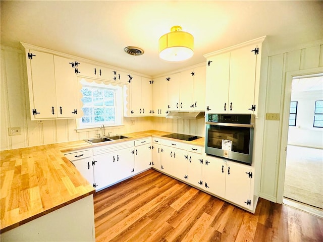 kitchen with black electric cooktop, wood counters, a sink, stainless steel oven, and plenty of natural light