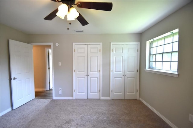 unfurnished bedroom with carpet flooring, two closets, and ceiling fan