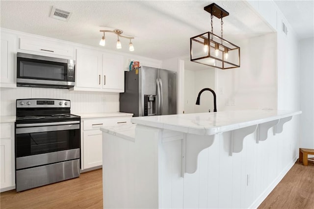 4017 Cottage Hill Rd Unit 17, Mobile, AL 36609 - kitchen with appliances with stainless steel finishes, light wood-type flooring, white cabinets, a peninsula, and a breakfast bar area