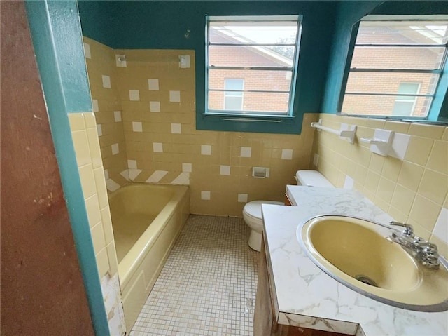 bathroom with toilet, tile walls, tile patterned floors, a bath, and vanity