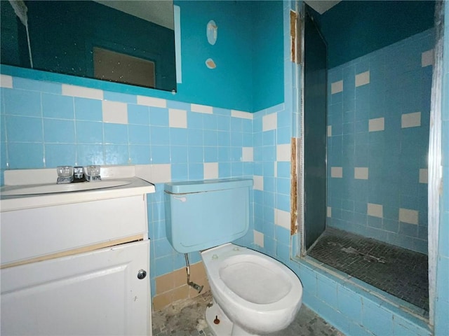 bathroom with toilet, a tile shower, tile walls, and vanity