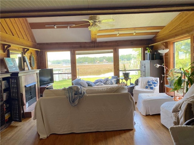 living room featuring light hardwood / wood-style flooring, ceiling fan, vaulted ceiling with beams, and a tile fireplace