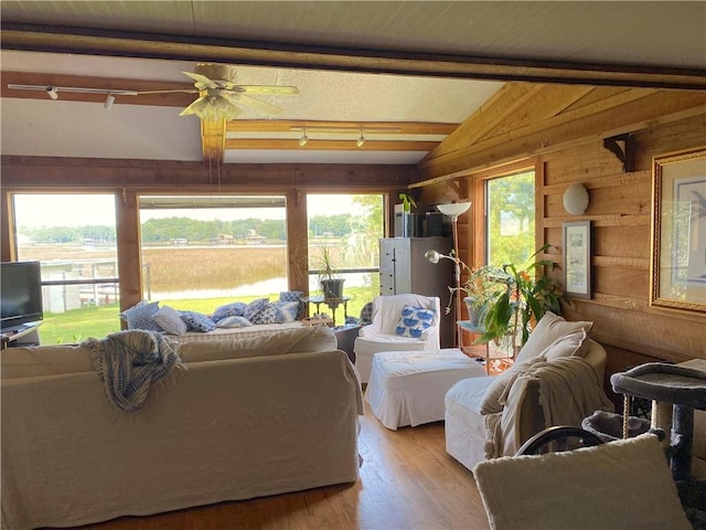 living room with ceiling fan, wooden walls, light hardwood / wood-style flooring, track lighting, and lofted ceiling with beams