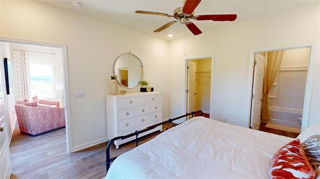 bedroom with hardwood / wood-style flooring, ceiling fan, a walk in closet, and ensuite bath