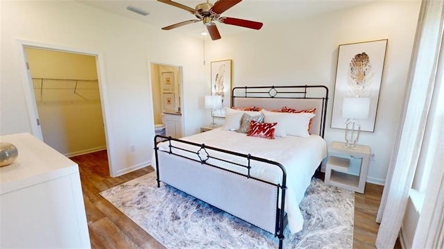 bedroom featuring a spacious closet, wood-type flooring, ensuite bath, and ceiling fan