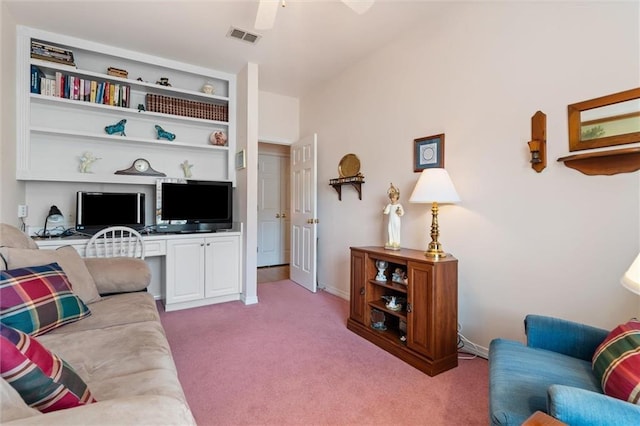 living room featuring built in desk, light carpet, ceiling fan, and built in shelves