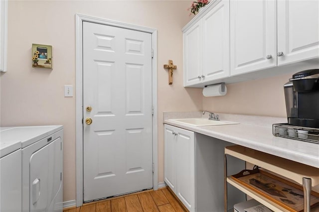 clothes washing area featuring cabinets, sink, washer and dryer, and light hardwood / wood-style flooring