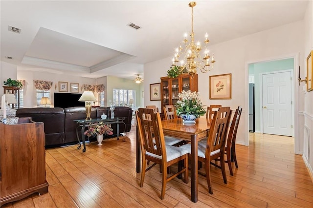 dining space with ceiling fan with notable chandelier, light hardwood / wood-style floors, and a tray ceiling