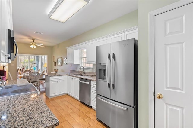 kitchen with appliances with stainless steel finishes, light stone countertops, light hardwood / wood-style floors, and white cabinets