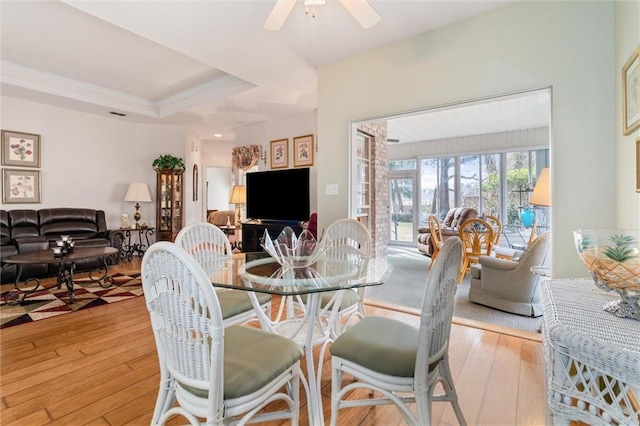 dining space featuring ceiling fan, ornamental molding, a raised ceiling, and light hardwood / wood-style floors