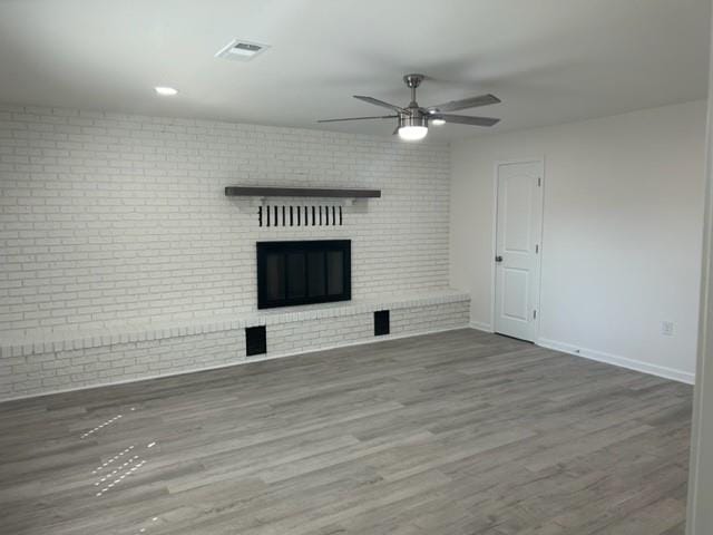 unfurnished living room featuring brick wall, dark wood-type flooring, a fireplace, and ceiling fan