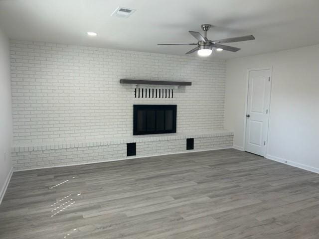 unfurnished living room with brick wall, a brick fireplace, wood-type flooring, and ceiling fan