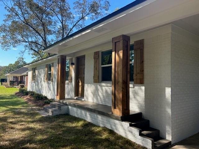 view of exterior entry featuring a porch and a lawn