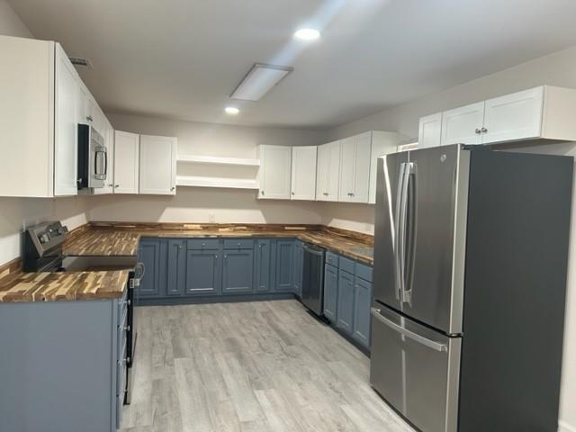 kitchen featuring white cabinets, blue cabinets, stainless steel appliances, and butcher block countertops