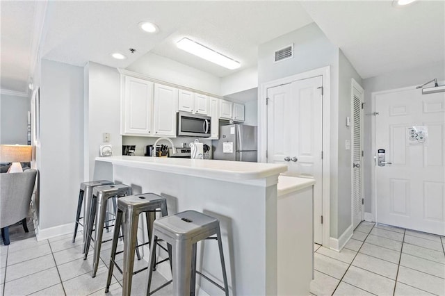 kitchen with a breakfast bar, white cabinets, appliances with stainless steel finishes, light tile patterned flooring, and kitchen peninsula