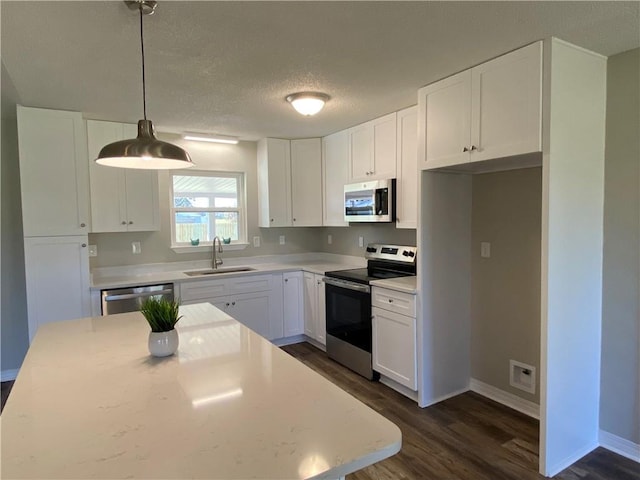 kitchen featuring appliances with stainless steel finishes, light countertops, white cabinetry, pendant lighting, and a sink