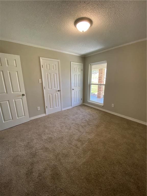 unfurnished bedroom featuring baseboards, ornamental molding, two closets, and carpet flooring