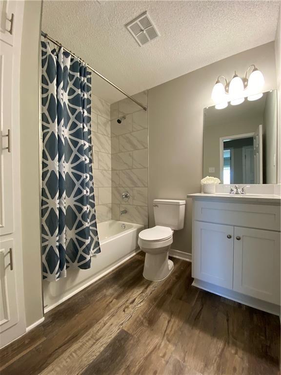 bathroom with visible vents, toilet, wood finished floors, shower / bath combo with shower curtain, and vanity