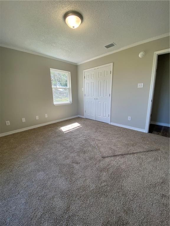 unfurnished bedroom with a textured ceiling, visible vents, baseboards, dark colored carpet, and crown molding