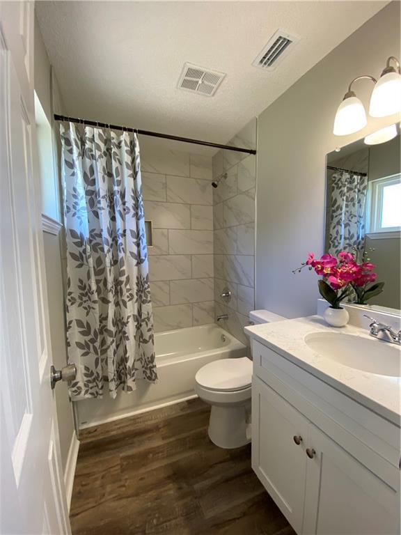 full bath with shower / tub combo, visible vents, wood finished floors, and vanity