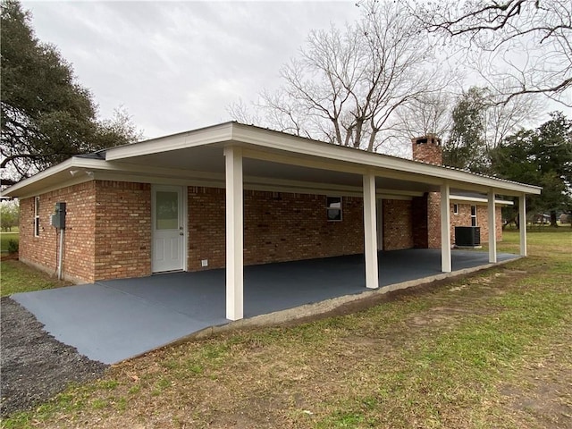 view of property exterior featuring a chimney, central AC unit, an attached carport, and brick siding