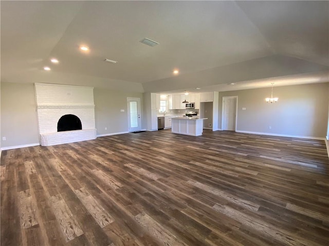 unfurnished living room featuring dark wood-style flooring, a fireplace, a notable chandelier, visible vents, and baseboards