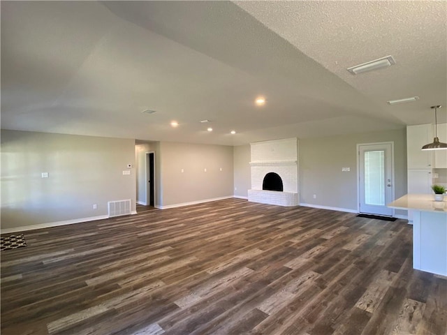 unfurnished living room with a brick fireplace, baseboards, visible vents, and dark wood-style flooring