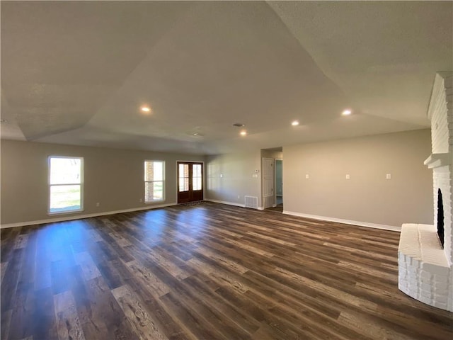 unfurnished living room featuring visible vents, a fireplace, baseboards, and dark wood finished floors