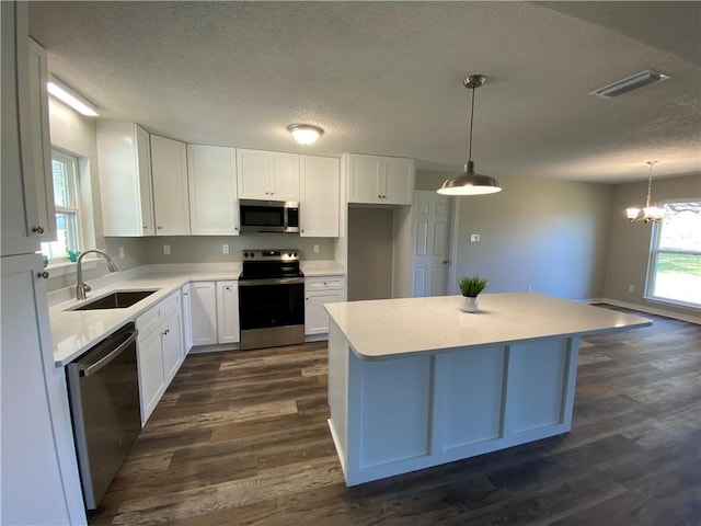 kitchen featuring stainless steel appliances, light countertops, white cabinets, and hanging light fixtures