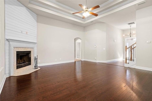 unfurnished living room featuring dark wood-type flooring, a high end fireplace, a raised ceiling, crown molding, and ceiling fan