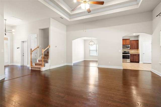 unfurnished living room with a raised ceiling, a towering ceiling, ceiling fan with notable chandelier, and dark hardwood / wood-style floors