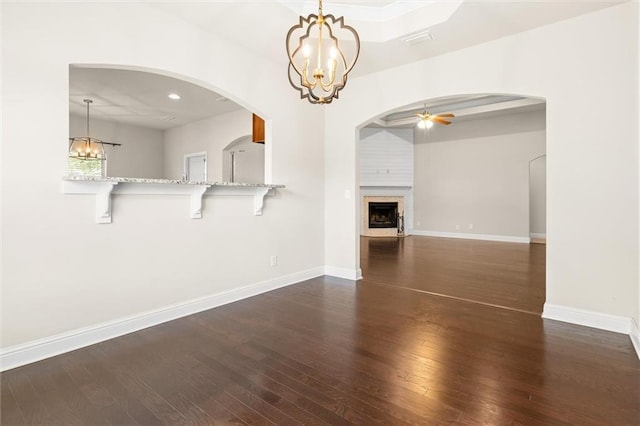 unfurnished living room with ceiling fan with notable chandelier and dark hardwood / wood-style floors