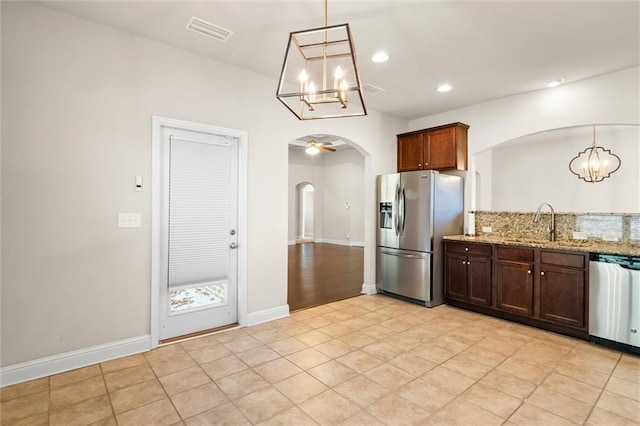 kitchen with appliances with stainless steel finishes, light stone counters, ceiling fan with notable chandelier, sink, and decorative light fixtures