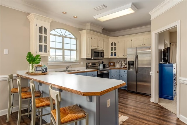 kitchen with appliances with stainless steel finishes, dark wood-type flooring, a kitchen bar, sink, and kitchen peninsula