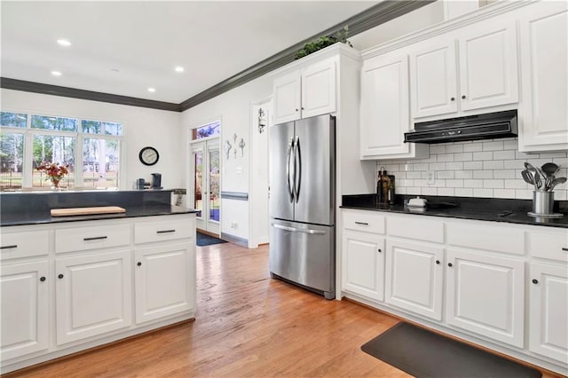 kitchen with tasteful backsplash, dark countertops, ornamental molding, freestanding refrigerator, and under cabinet range hood