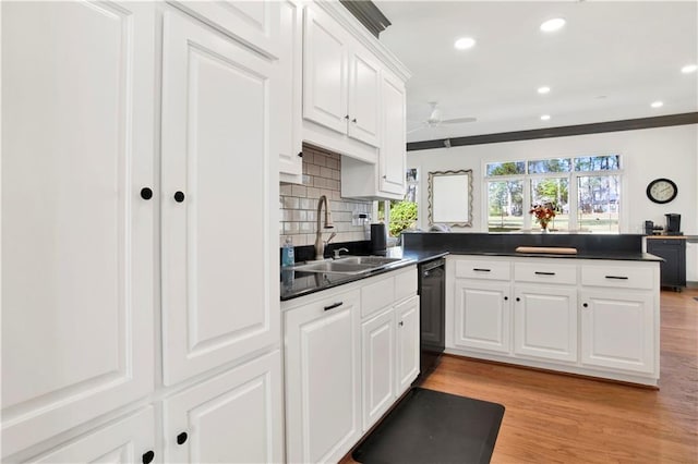 kitchen with a peninsula, dark countertops, black dishwasher, and a sink