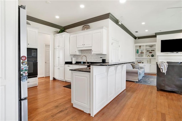 kitchen with black appliances, white cabinetry, open floor plan, and a sink