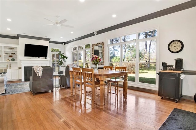 dining space with built in shelves, light wood-style flooring, recessed lighting, a fireplace, and crown molding